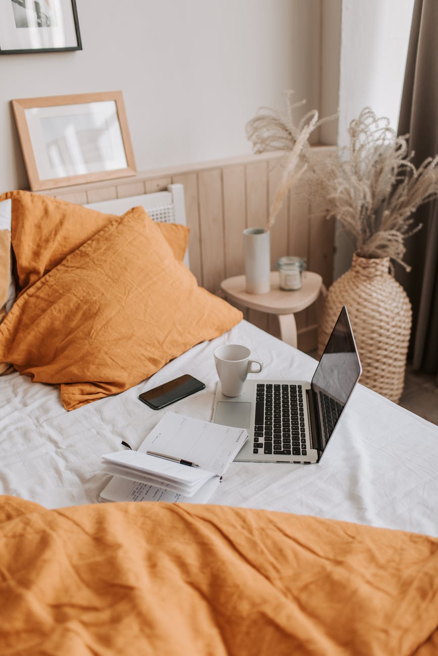 laptop with copybook and cup of coffee on bed sheet