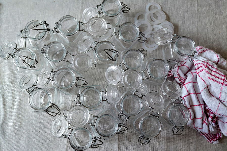 Viele kleine Gläser mit Bügelverschluss und Weiß-rot-kariertes Geschirrtuch
