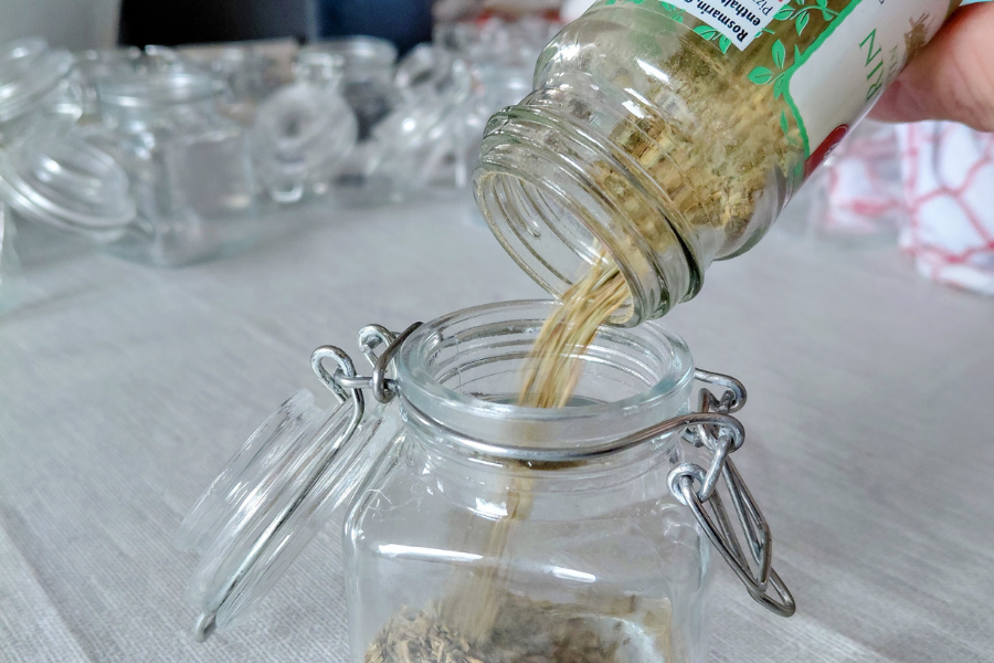 Aus einem Gewürzglas wird Rosmarin in ein neues Glas umgefüllt.